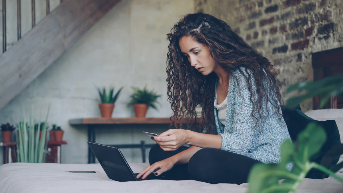 A young woman sitting on her bed with a laptop, holding a payment card while shopping online