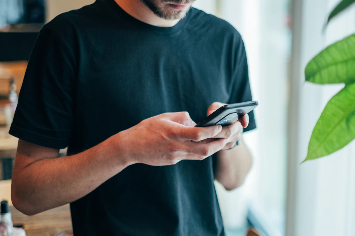 A man in a dark T-shirt using his smartphone indoors